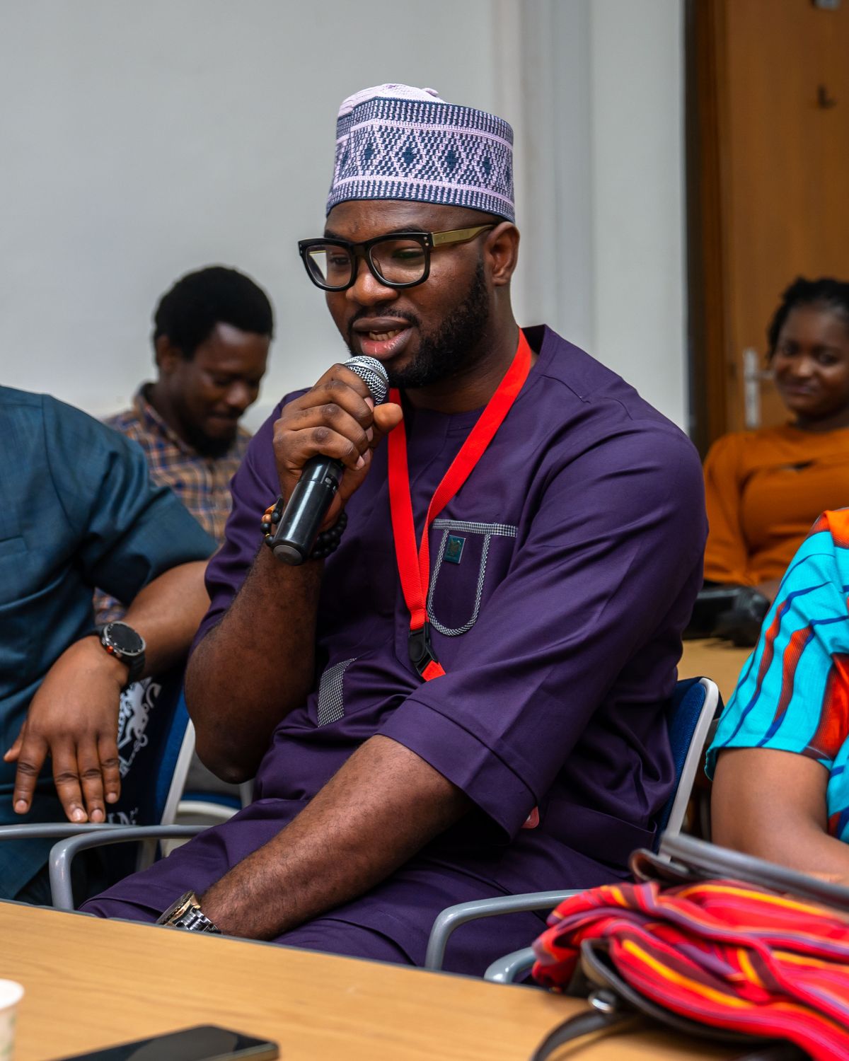 Abraham Ologundudu speaking into a microphone, seated among delegates